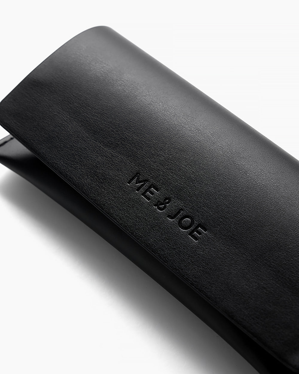 Close-up of black ME & JOE eyewear case with embossed logo