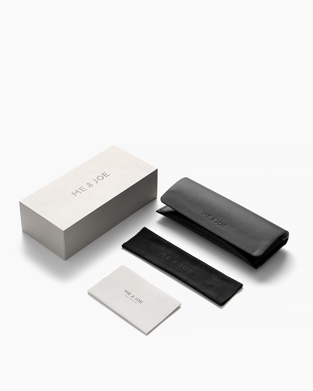 ME & JOE eyewear packaging set including box, glasses case, cleaning cloth, and booklet in a minimal black and white design