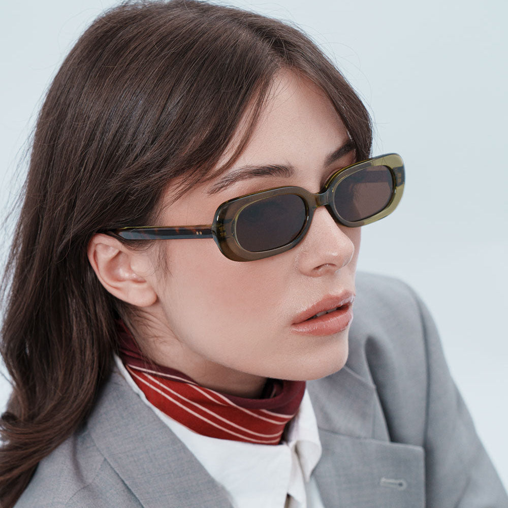 Woman wearing sunglasses and a gray blazer with a white shirt and red scarf.