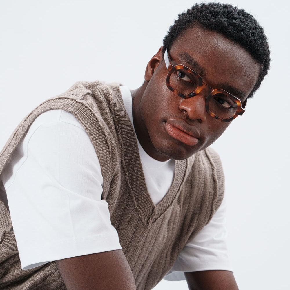 Man wearing a brown vest over a white shirt with a neutral background