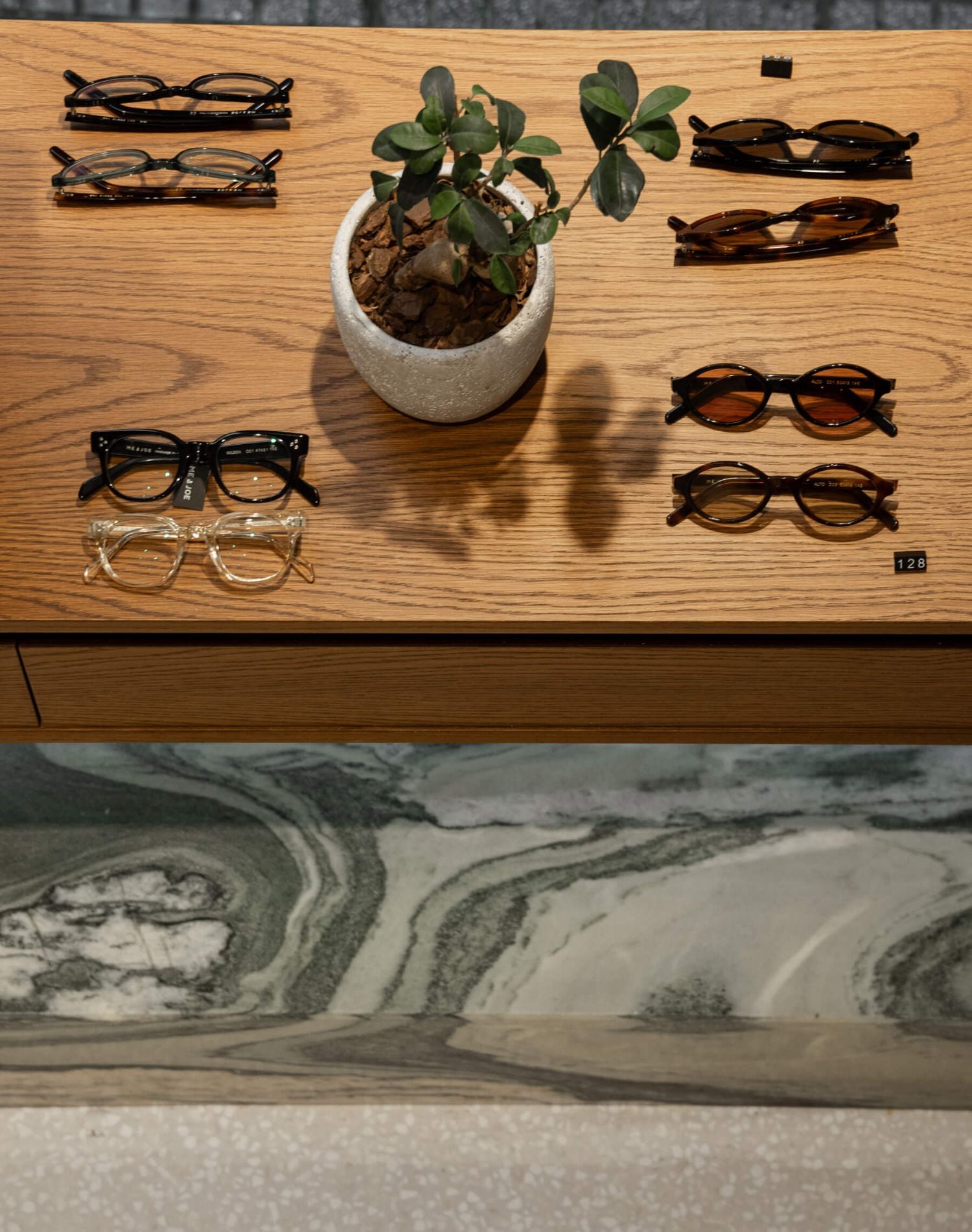 Display table with ME & JOE optical and sunglasses arranged beside a small plant inside the Tsimiski store