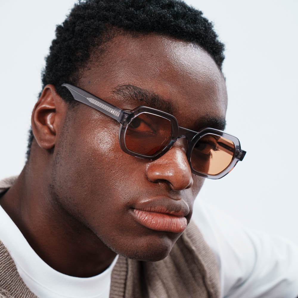 Man wearing sunglasses and a brown cardigan against a light background
