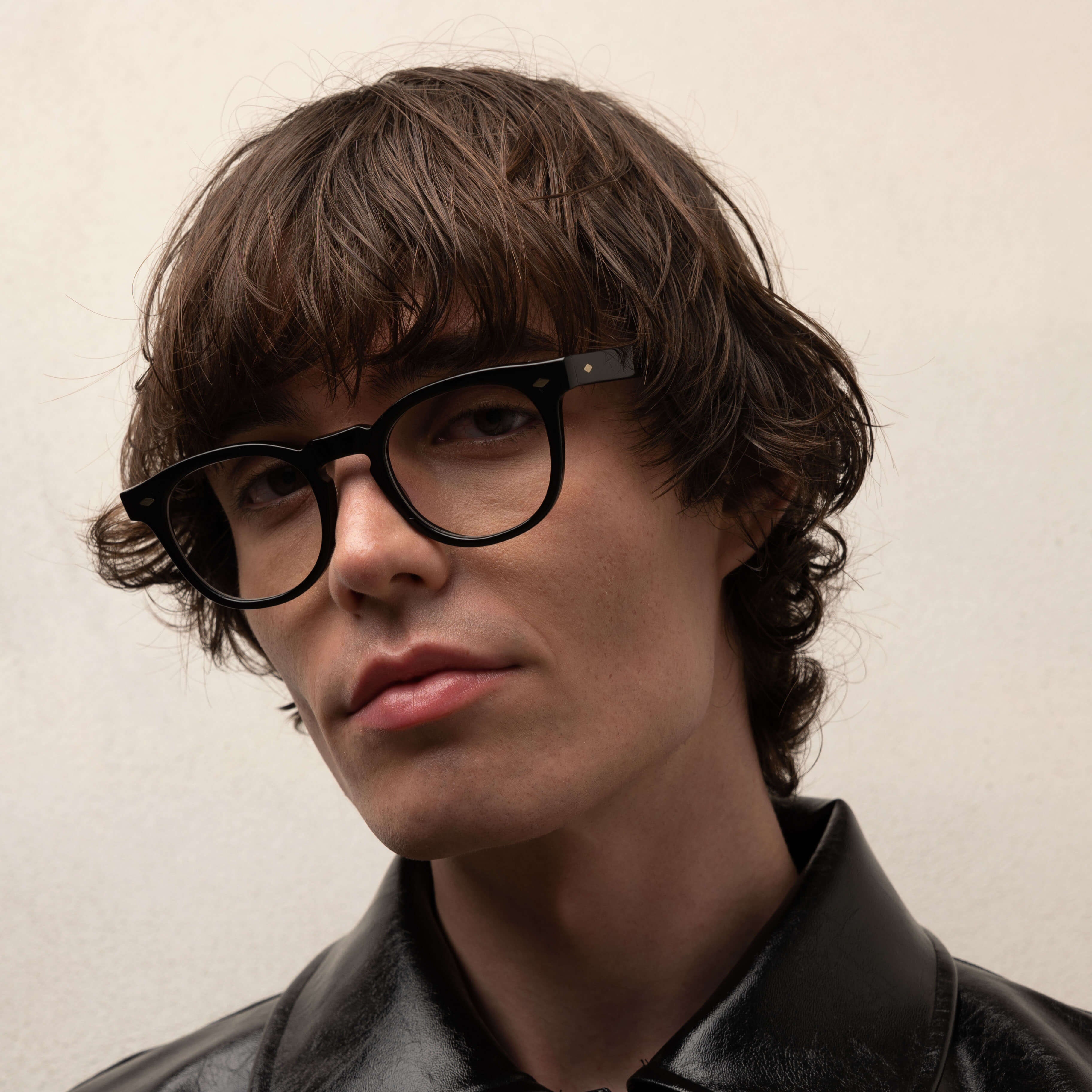 Person wearing a black leather jacket and glasses against a plain background