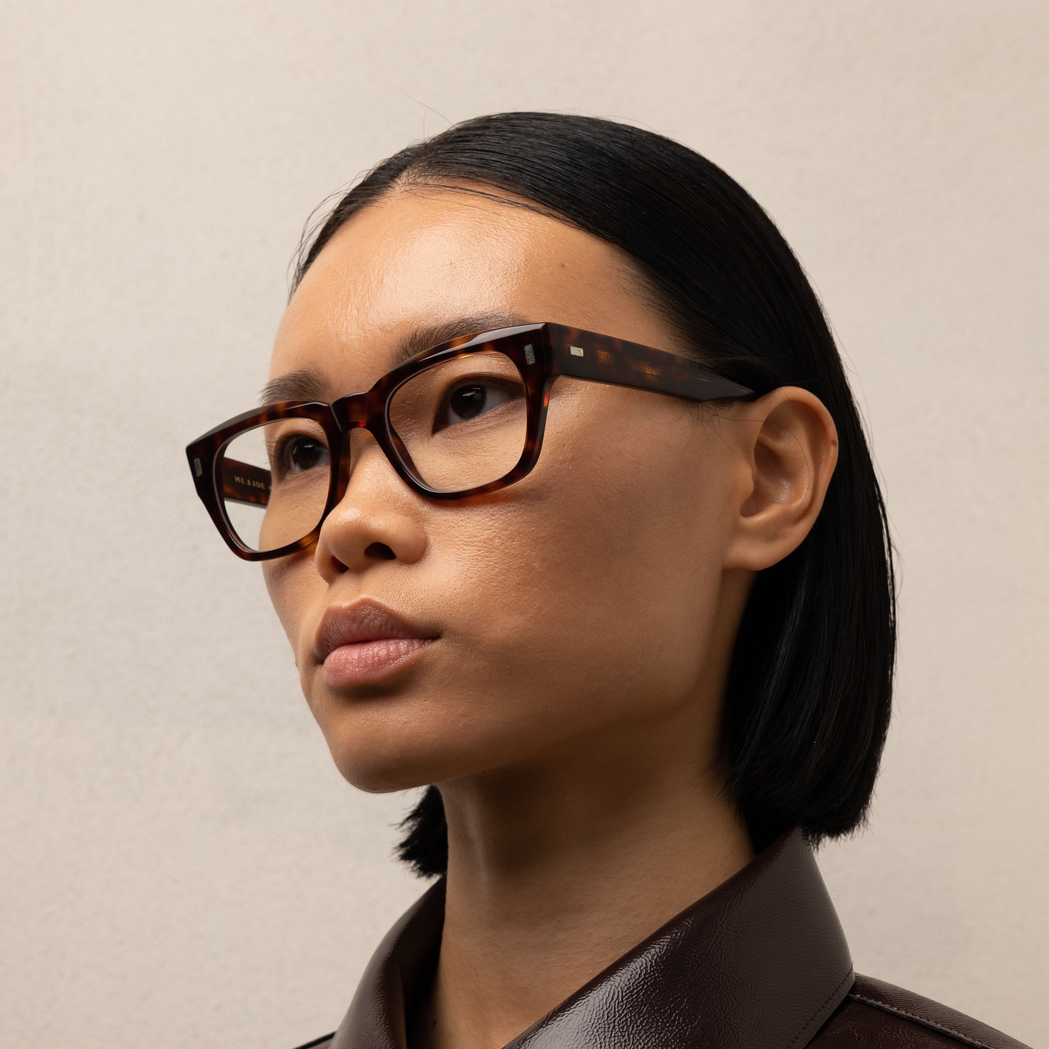 Person wearing glasses and a brown leather shirt against a neutral background